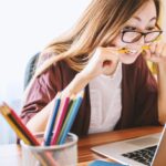 Fille mord un stylo devant son ordinateur