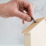Main mettant une pièce dans une maison tirelire