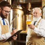 Two workers of brewery examining craft beer.
