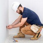 Electrician Builder at work, installation of sockets and switches. Professional in overalls with an electrician’s tool. Against the background of the repair site.
