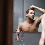Young Man In Bathroom Worried About Premature Receding Hairline