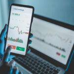 Trader using stock exchange app online for trading operations in mobile phone – Focus on left hand holding smartphone