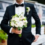Wedding bouquet at hand of groom with bow tie