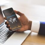 Black businessman checking global financial analytic on smartphone or trading on forex