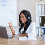 Telecommuting concept. Smiling African American woman with headphones working online on laptop at office