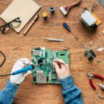 cropped image of electronic engineer with prosthetic arm fixing motherboard by soldering iron and