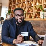 The time making money should be greater than the time that you are spending money. Smiling african american businessman holds his credit card, while resting in the cafe